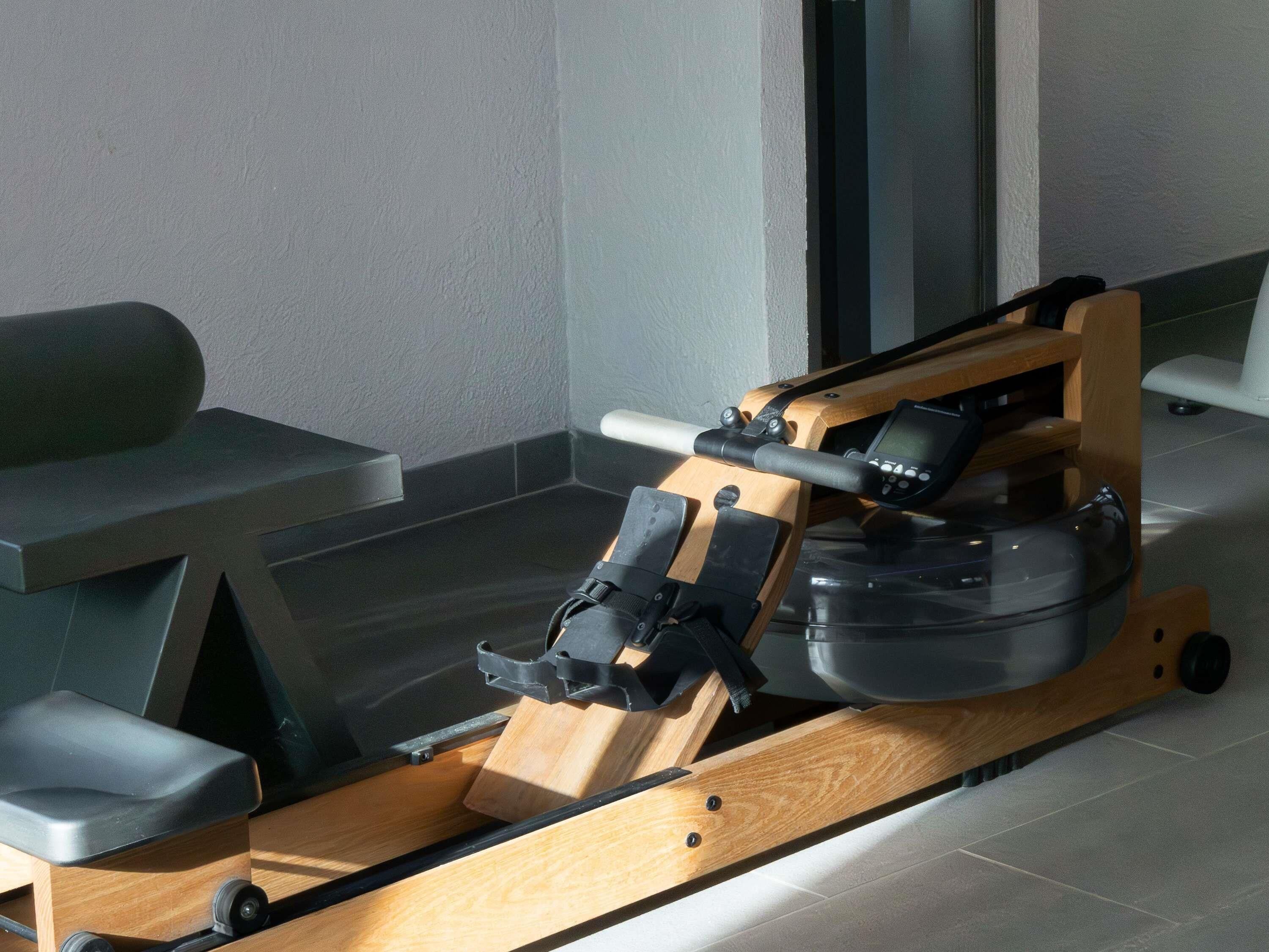Una máquina de remo en una habitación con ventana, un banco y suelo de baldosas.