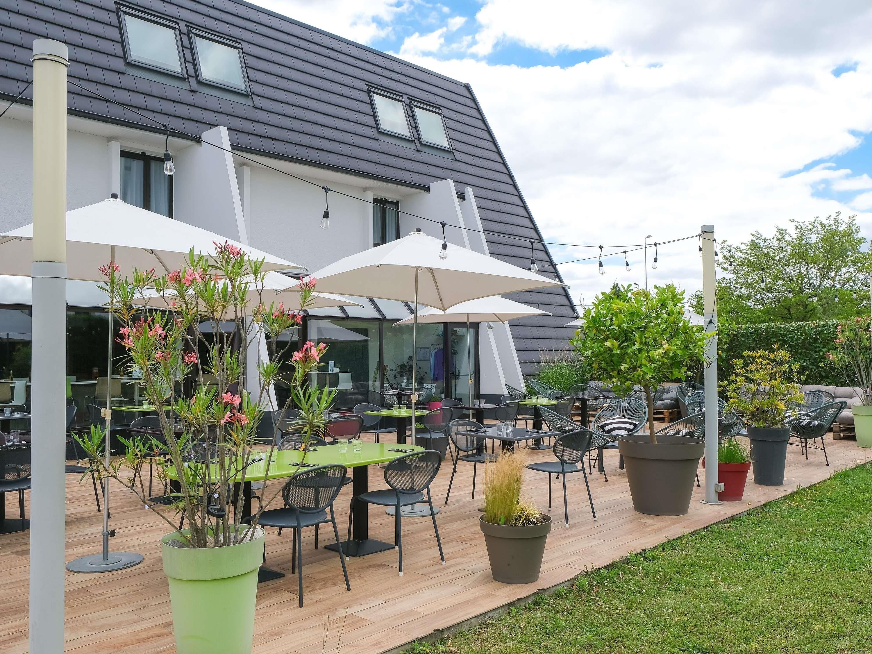 An outdoor patio with tables and chairs, surrounded by potted plants and umbrellas.