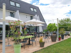 Un patio al aire libre con mesas y sillas, rodeado de plantas en macetas y sombrillas.