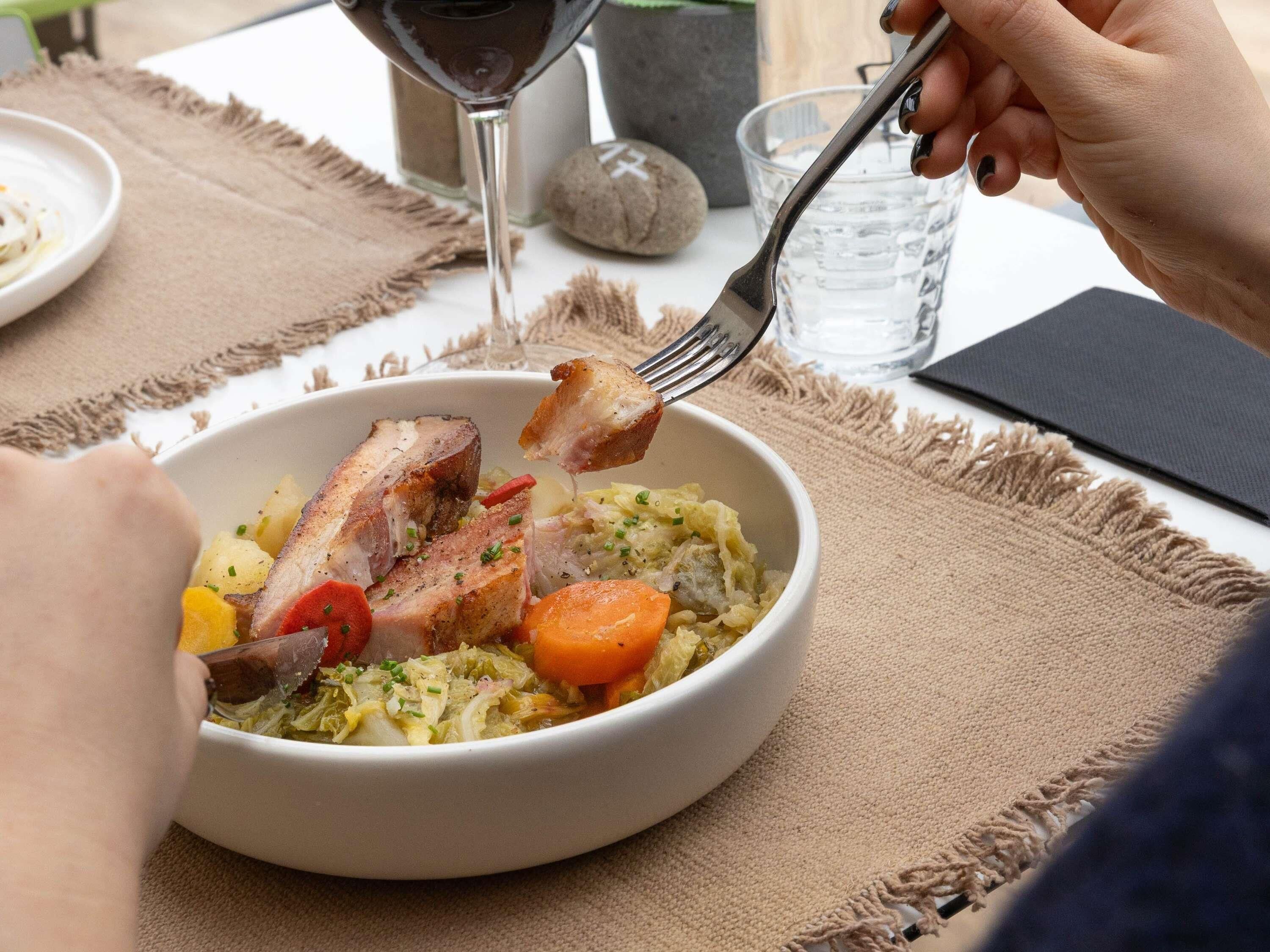 A bowl of food with a fork, a glass of water, and a wine glass on a table with a placemat.