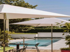A poolside area with a covered seating area, a pool, and surrounding greenery.