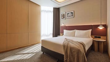 A hotel room with a large bed, a bedside table, a lamp, and a view of the outside through the window.