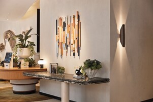 Una zona de recepción con mostrador de mármol, plantas en macetas, una obra de arte en la pared y una lámpara moderna.