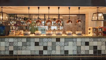 A kitchen counter with various cooking utensils and appliances, a tiled backsplash, and hanging copper pendant lights.