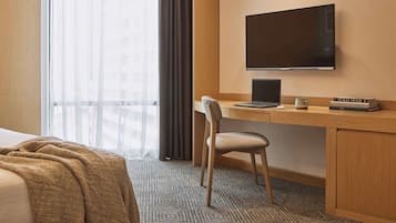 A hotel room with a bed, a desk with a laptop, a TV, and a window with curtains.