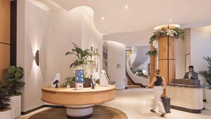 Rebedor modern d'hotel amb una recepció central, una escala corba i plantes en testos.