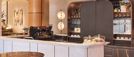 A modern bar area with a coffee machine, seating, and a wine and glass display.