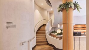 Un hall d'hotel modern amb una escala de fusta, una recepció i un senyal que indica la ubicació del restaurant i la sala de reunions.
