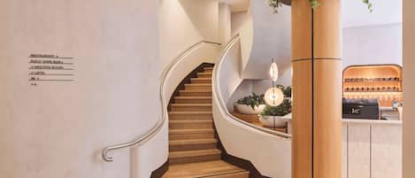 Un moderno vestíbulo de hotel con una escalera de madera, una recepción y un letrero que indica la ubicación del restaurante y la sala de reuniones.