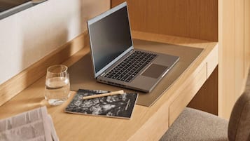 Una computadora portátil sobre un escritorio de madera con un vaso de agua, una revista y un bolígrafo.