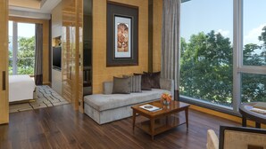 A modern living room with a sofa, coffee table, and a large window offering a view of trees. - The Olympian Hong Kong (Kowloon)