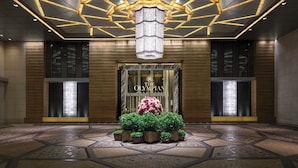 A hotel lobby with a geometric ceiling design, a central column, and a floral arrangement. - The Olympian Hong Kong (Kowloon)