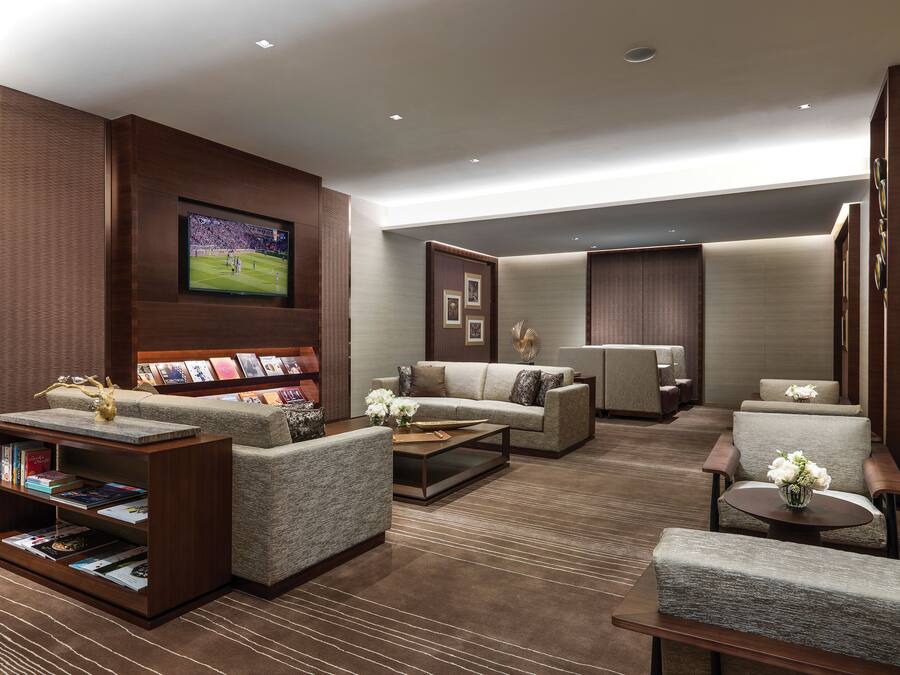 A modern hotel lobby with a large flat-screen TV, comfortable seating, a bookshelf, and a decorative wall panel.