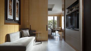 Sala de estar moderna com sofá, mesa de centro e TV fixada na parede. Uma grande janela oferece luz natural e vista para o exterior.