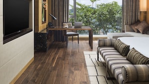 A modern hotel room with a large flat-screen TV, a desk with a laptop, a comfortable sofa, and a large window offering a view of greenery. - The Olympian Hong Kong (Kowloon)