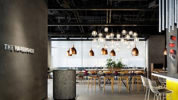 A modern restaurant interior with a central dining area, hanging spherical light fixtures, and a sign reading "THE WAREHOUSE".