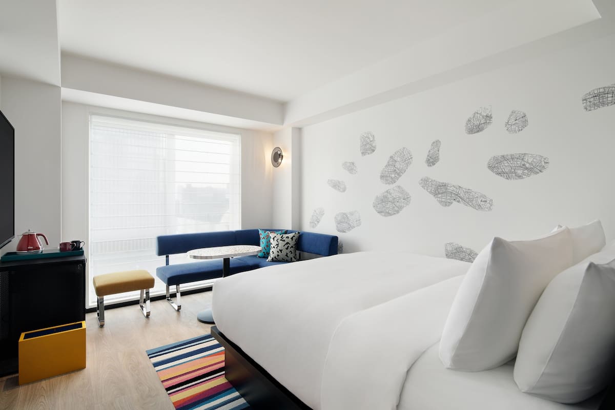 Una camera d'albergo moderna con un letto grande, un divano blu, un tavolino e un tappeto colorato a righe.