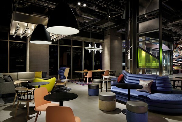 Ein stilvoller Lounge-Bereich mit Sofas, Sesseln und Tischen, ausgestattet mit großen Fenstern und einer sichtbaren Treppe.