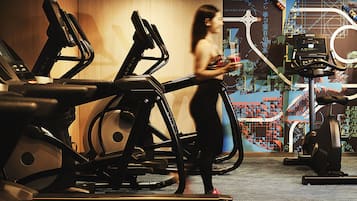 Una palestra con tapis roulant e attrezzature per esercizi, una donna che cammina e un grande murale sulla parete.