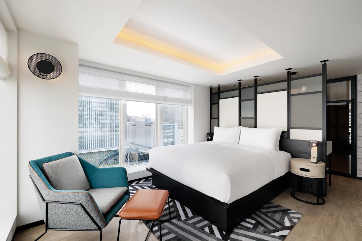 A modern hotel room with a large bed, a seating area, a nightstand, and a view of the city.