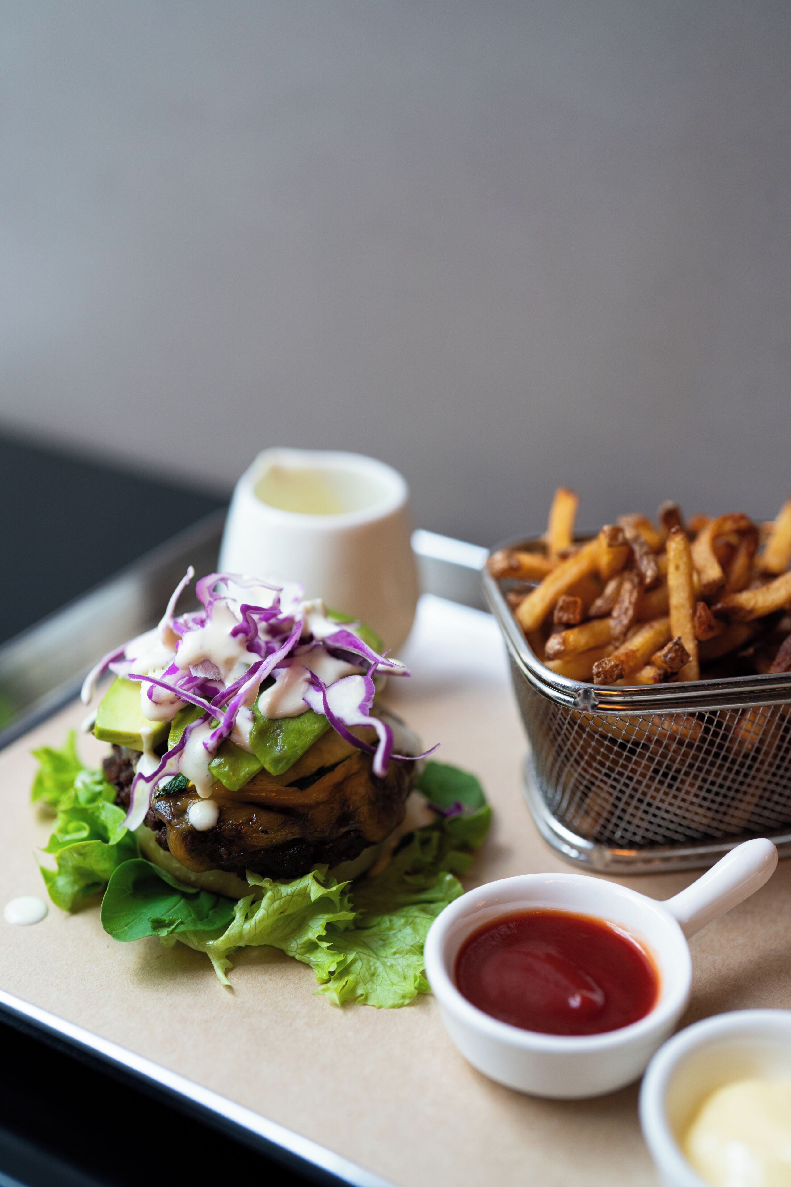 A burger with lettuce, a side of fries, and two dipping sauces.