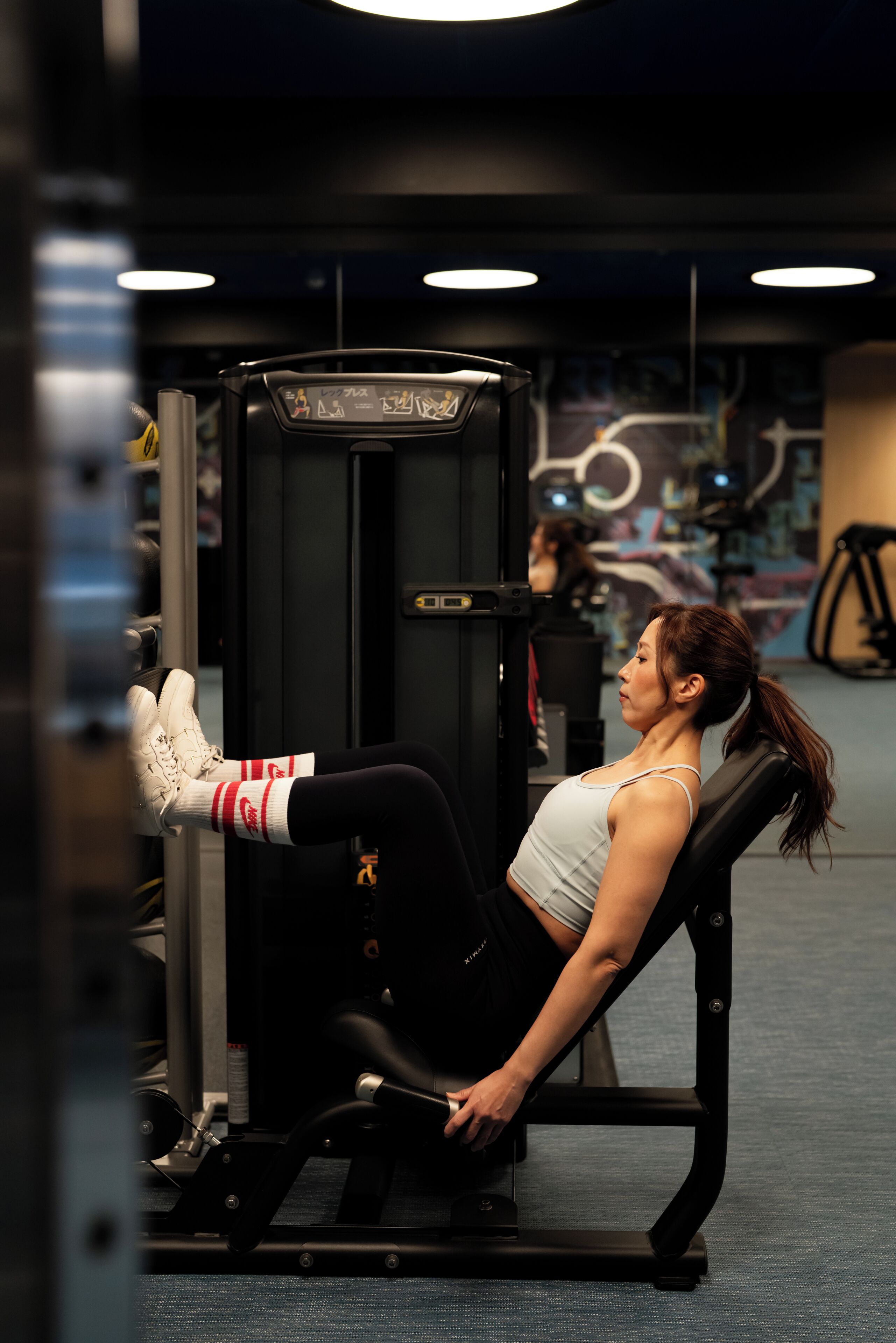 A person using a leg press machine in a gym with exercise equipment and a wall with graffiti.