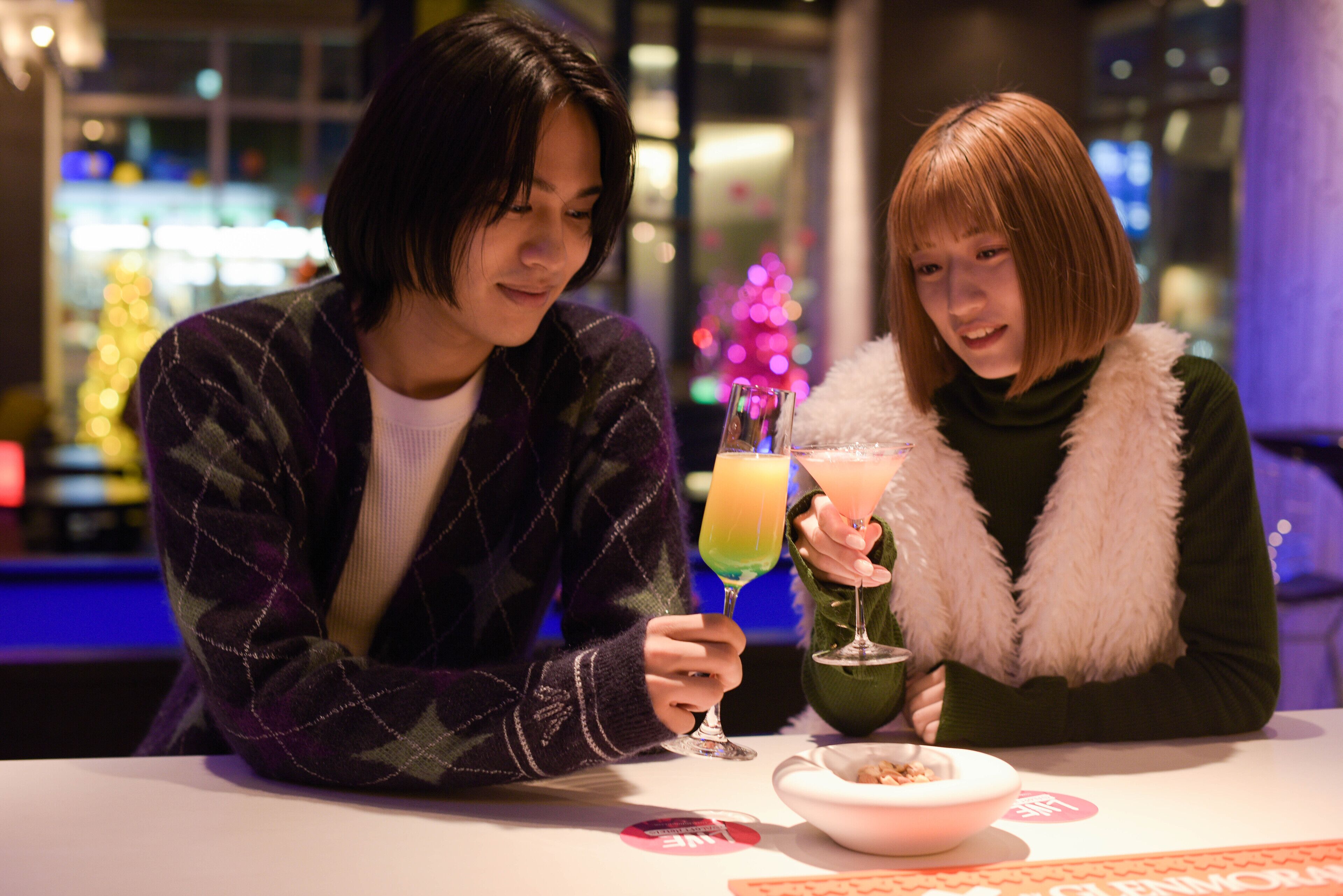 Two people sitting at a table with drinks and a bowl of cereal.