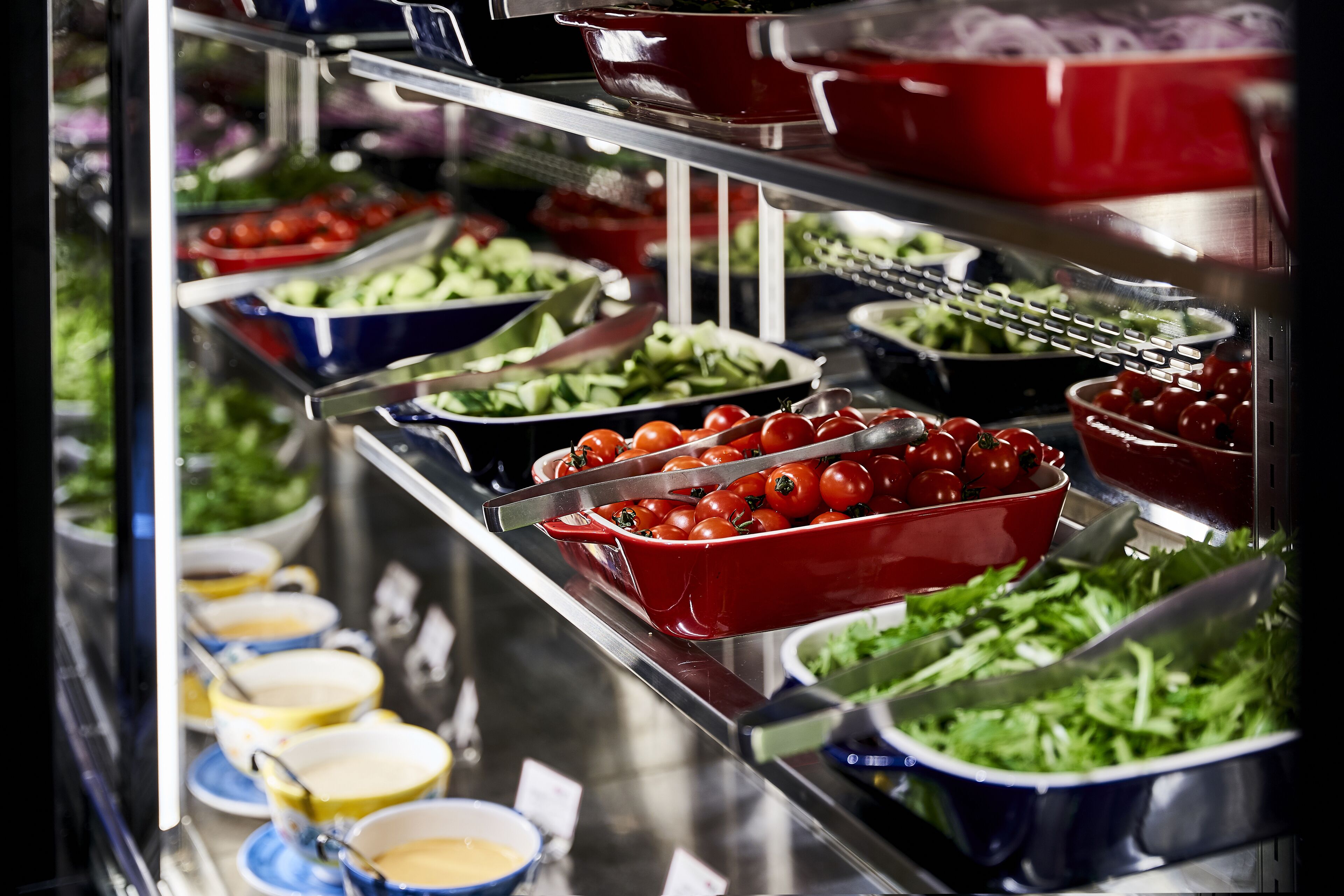 A buffet with various food items including salads, tomatoes, and bowls of soup.