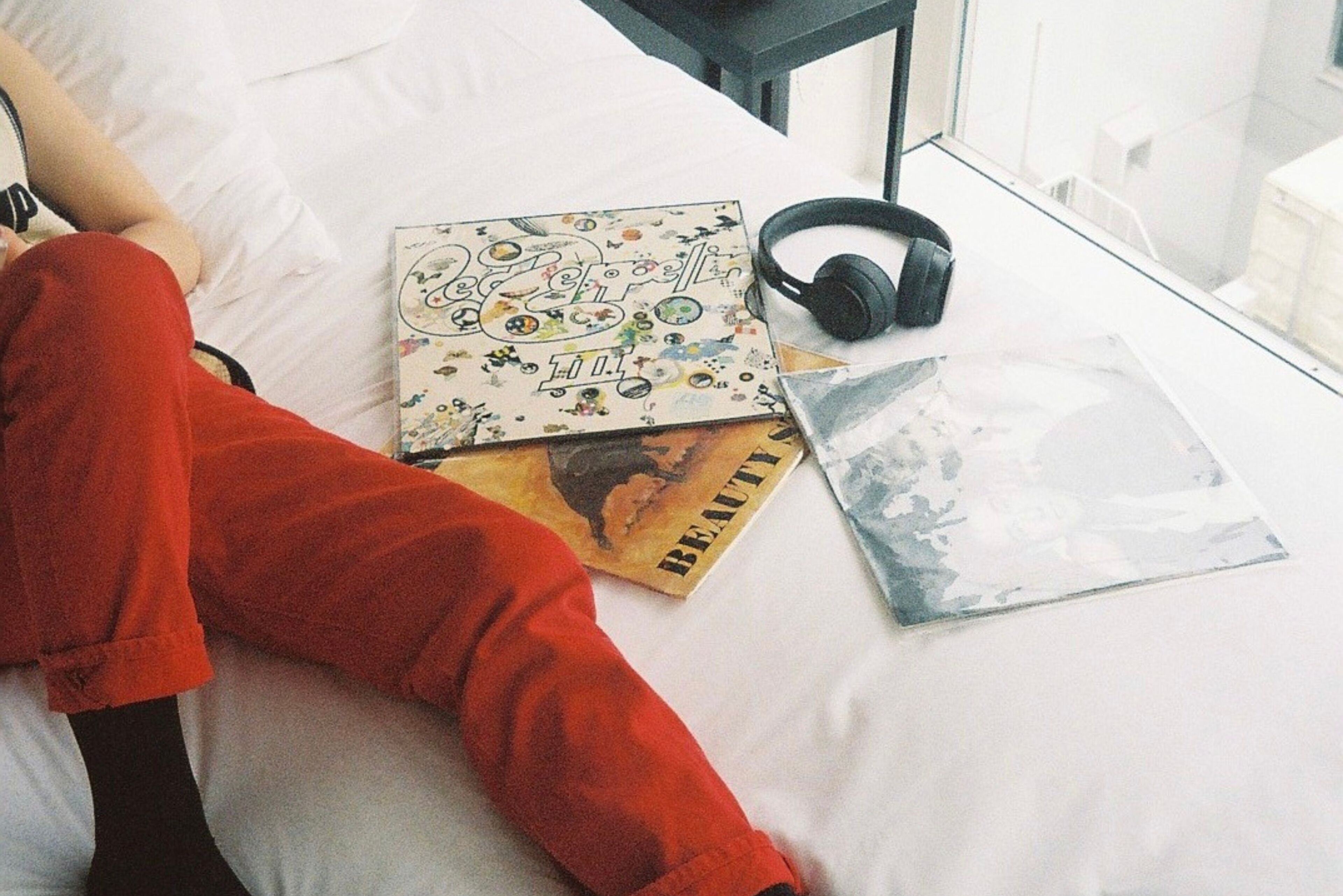 A bed with a white comforter, a pair of headphones, and a few books on it.