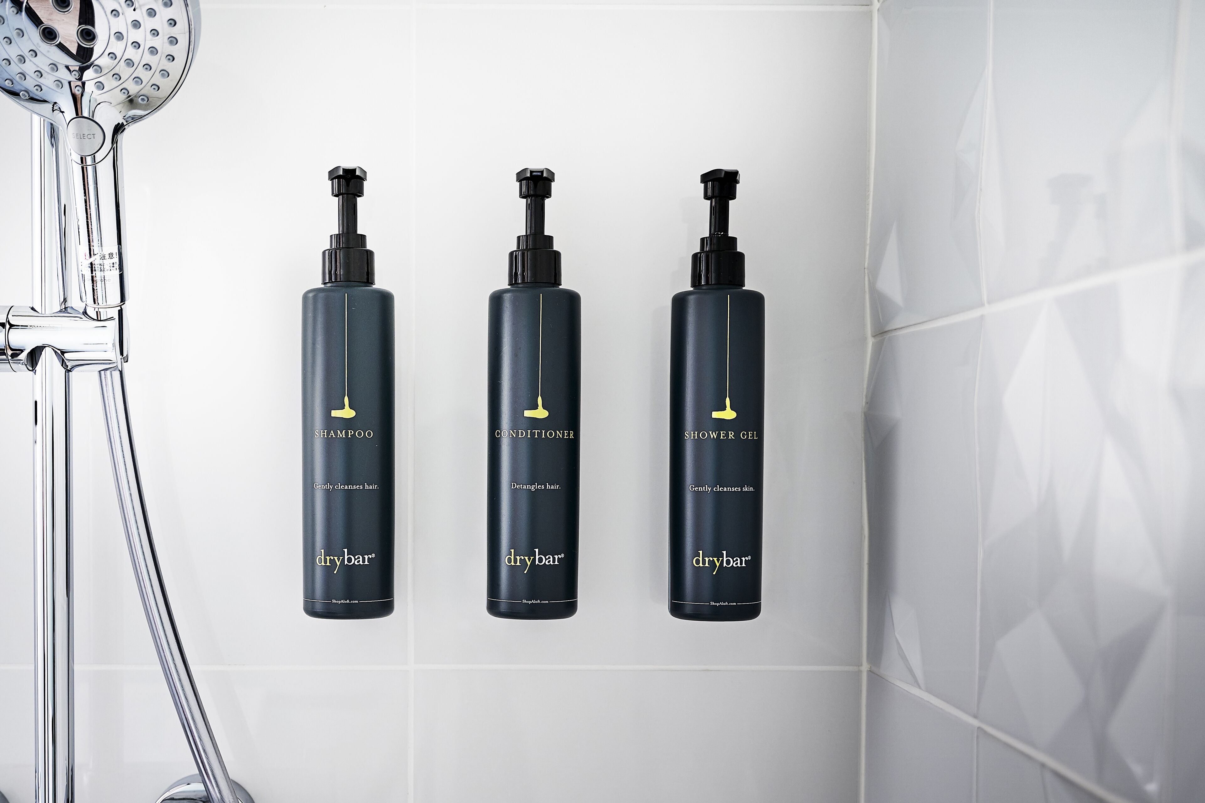 Un baño con ducha, inodoro de pared y tres productos de drybar.