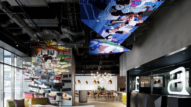 Et moderne interiør med en væg fyldt med skateboards, et spiseområde og en reception.
