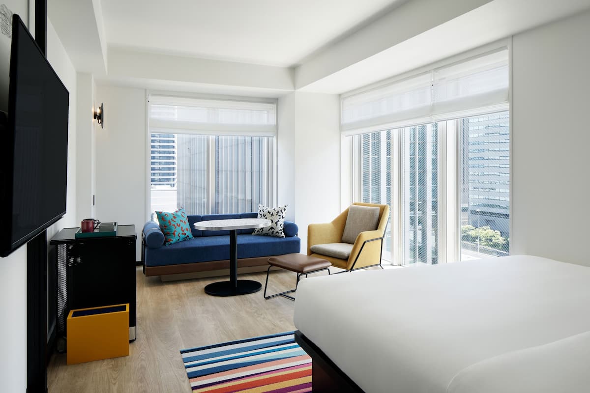 A modern hotel room with a large bed, a sofa, a chair, a small table, and a TV.