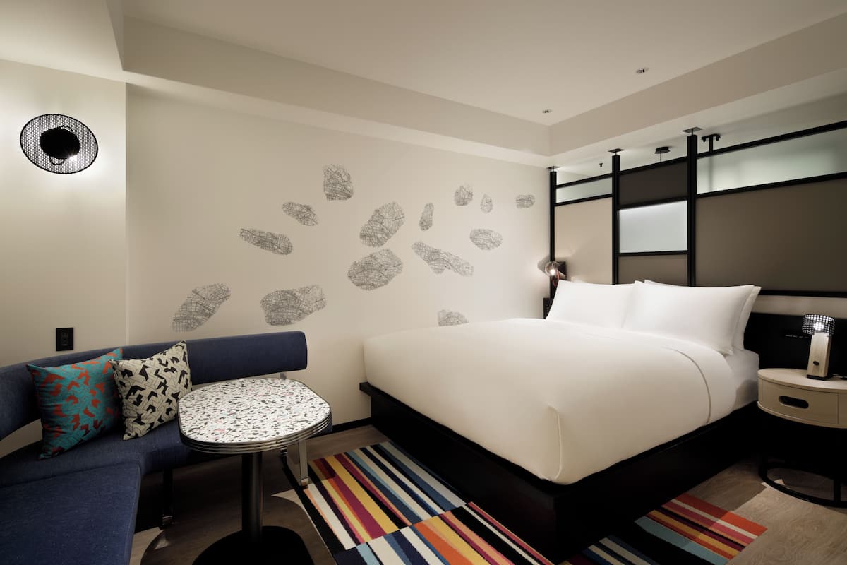 A modern hotel room with a large bed, a sofa, a small round table, and a colorful striped rug.