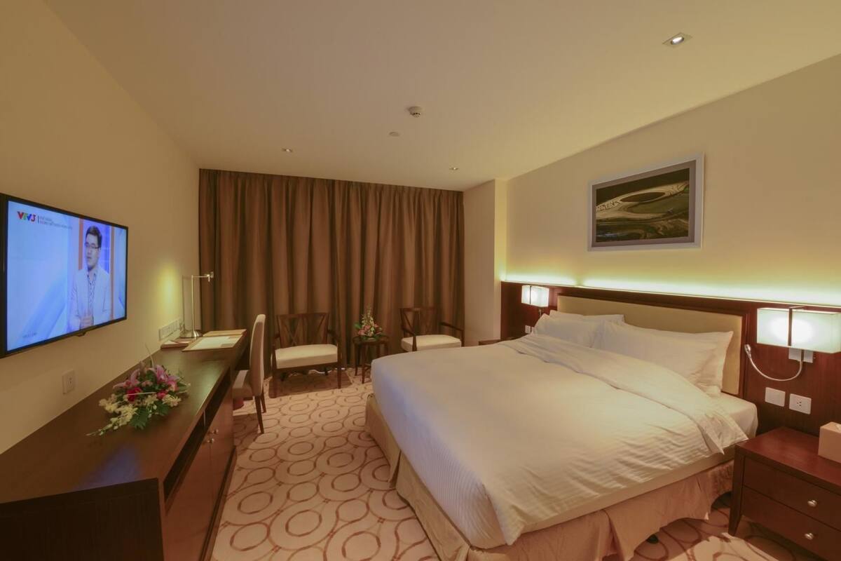 Hotelkamer met een groot bed, een bureau met een televisie, twee stoelen, een nachtkastje met een lamp en een schilderij aan de muur.