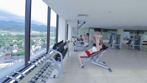 Un gimnasio con equipo de ejercicio, ventanas amplias y vistas a un paisaje urbano.