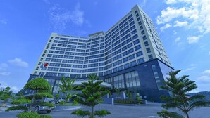 Un hotel moderno con un llamativo letrero 'ARISTO', que presenta una estructura de varios pisos, grandes ventanales y un jardín bien cuidado con diversas plantas.
