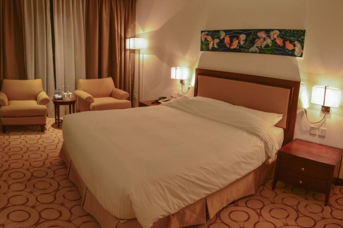 Een hotelkamer met een groot bed, twee fauteuils, een bureau met een televisie en een schilderij aan de muur.