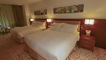 A hotel room with two beds, a desk, and a chair. There are paintings on the walls and a patterned carpet.