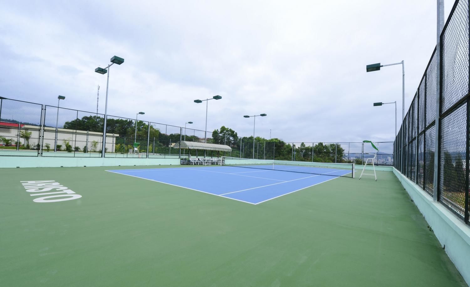 Un campo da tennis all'aperto con superficie verde, circondato da una recinzione e dotato di numerosi fari.
