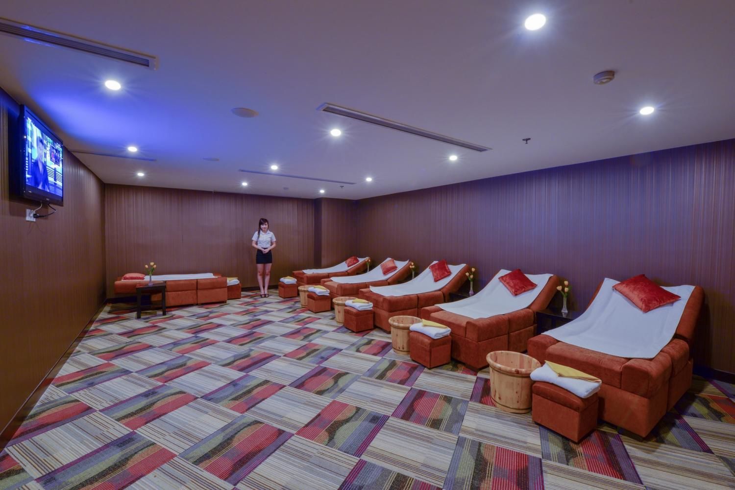 A room with multiple massage beds arranged in rows, a television on the wall, and a patterned carpet.