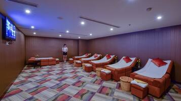 A room with multiple massage beds arranged in rows, a television on the wall, and a patterned carpet.