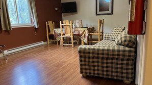 A cozy living room with a plaid sofa, wooden chairs, a dining table, and a flat-screen TV mounted on the wall. - Denali Rainbow Village RV Park and Motel (Denali National Park)