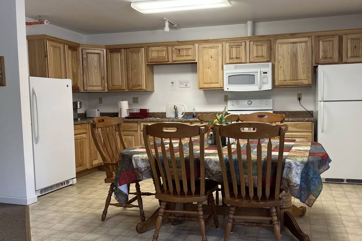 A compact kitchen with wooden cabinets, a microwave, a refrigerator, and a dining table with chairs.