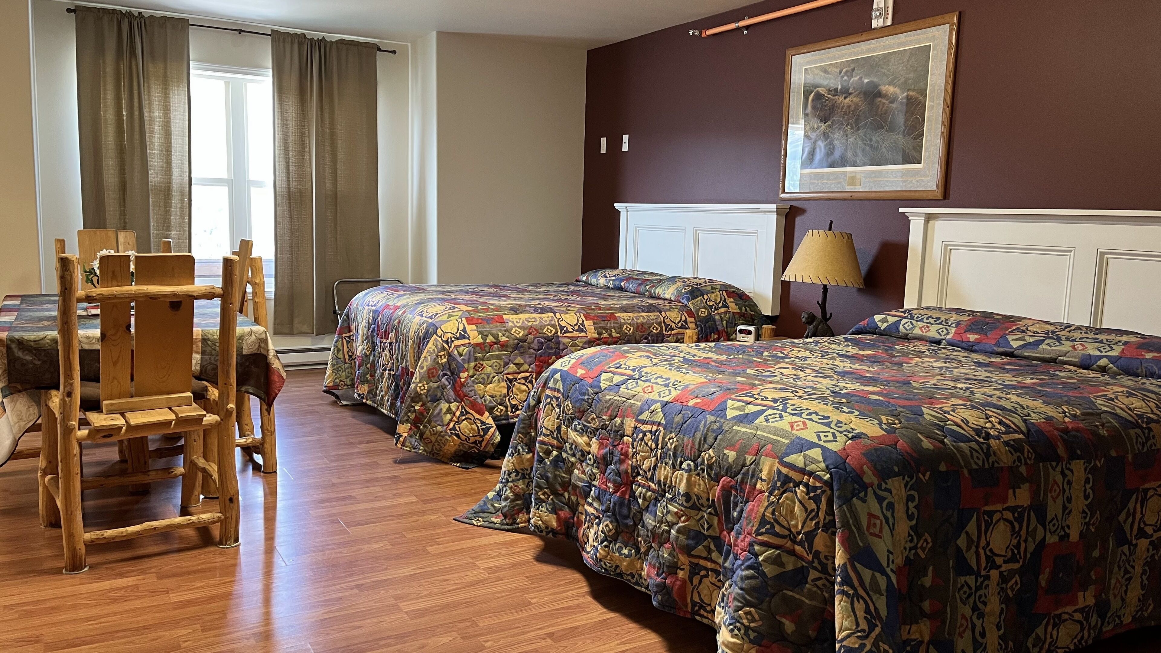 Une chambre d’hôtel avec deux lits, une chaise en bois, une lampe et un tableau au mur.