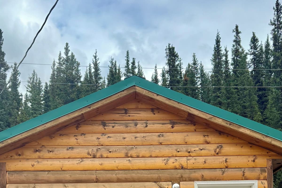 A log cabin with a green roof, a white door, and a wooden staircase leading to a porch.
