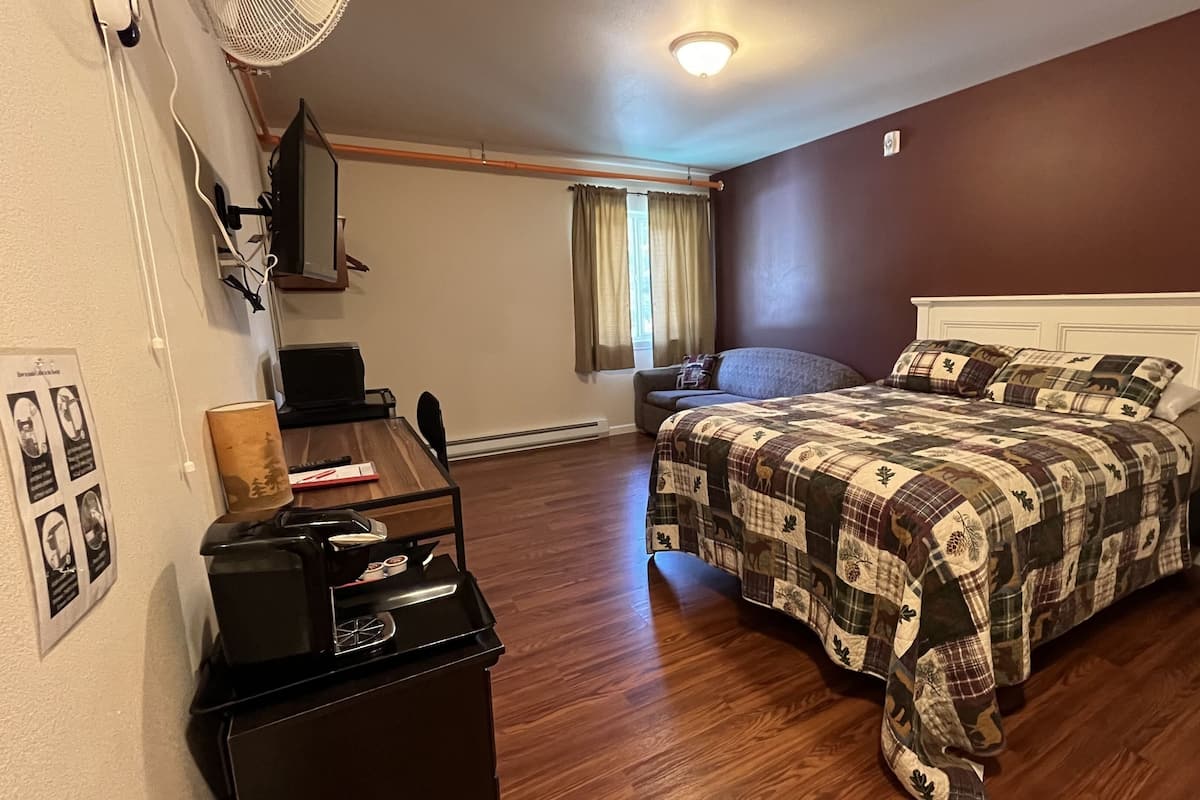 A bedroom with a bed, a desk, a chair, a lamp, and a window with curtains.