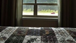 A room with a large bed, a window with a mountain view, and curtains. - Denali Rainbow Village RV Park and Motel (Denali National Park)