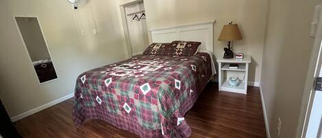 Un dormitorio con cama, mesita de noche, lámpara, reloj y espejo en la pared.