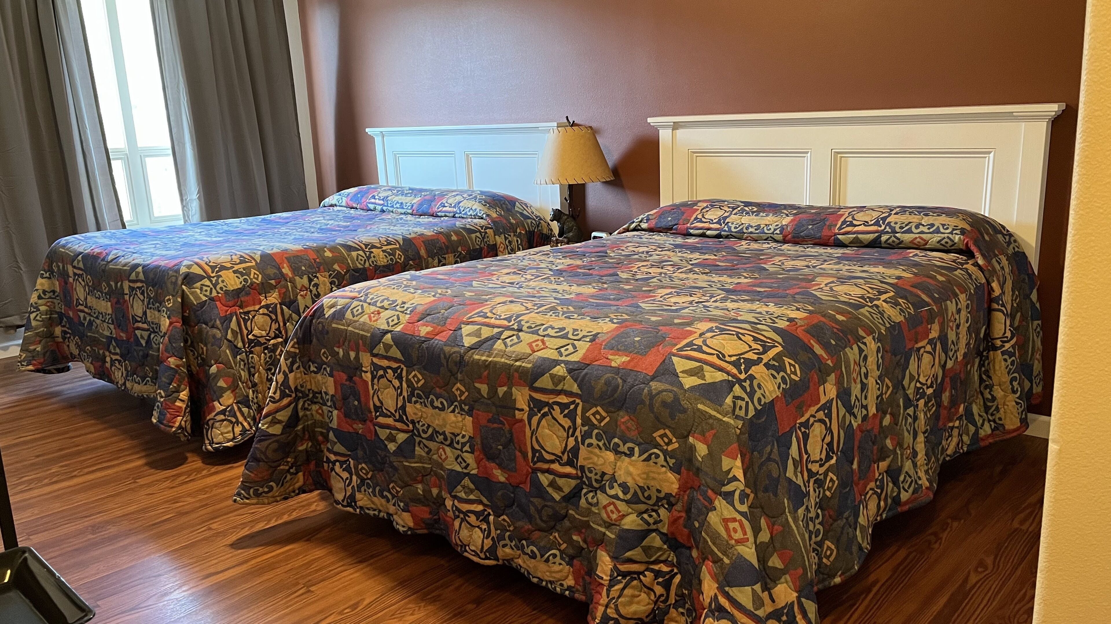 Dos camas con ropa de cama estampada, una lámpara de noche y un suelo de madera en una habitación de hotel.