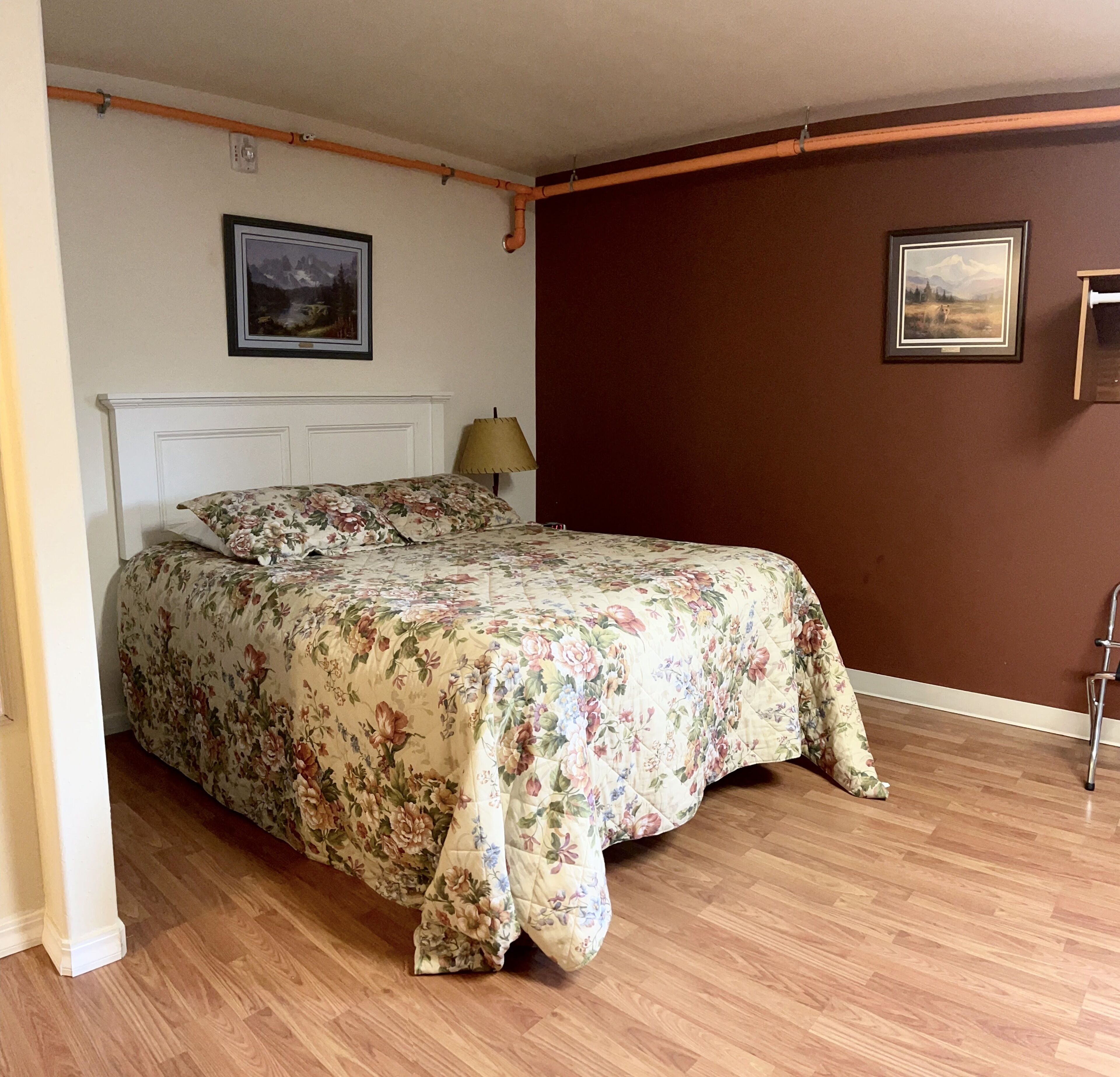 Un dormitorio con una cama, piso de madera y dos cuadros en las paredes.